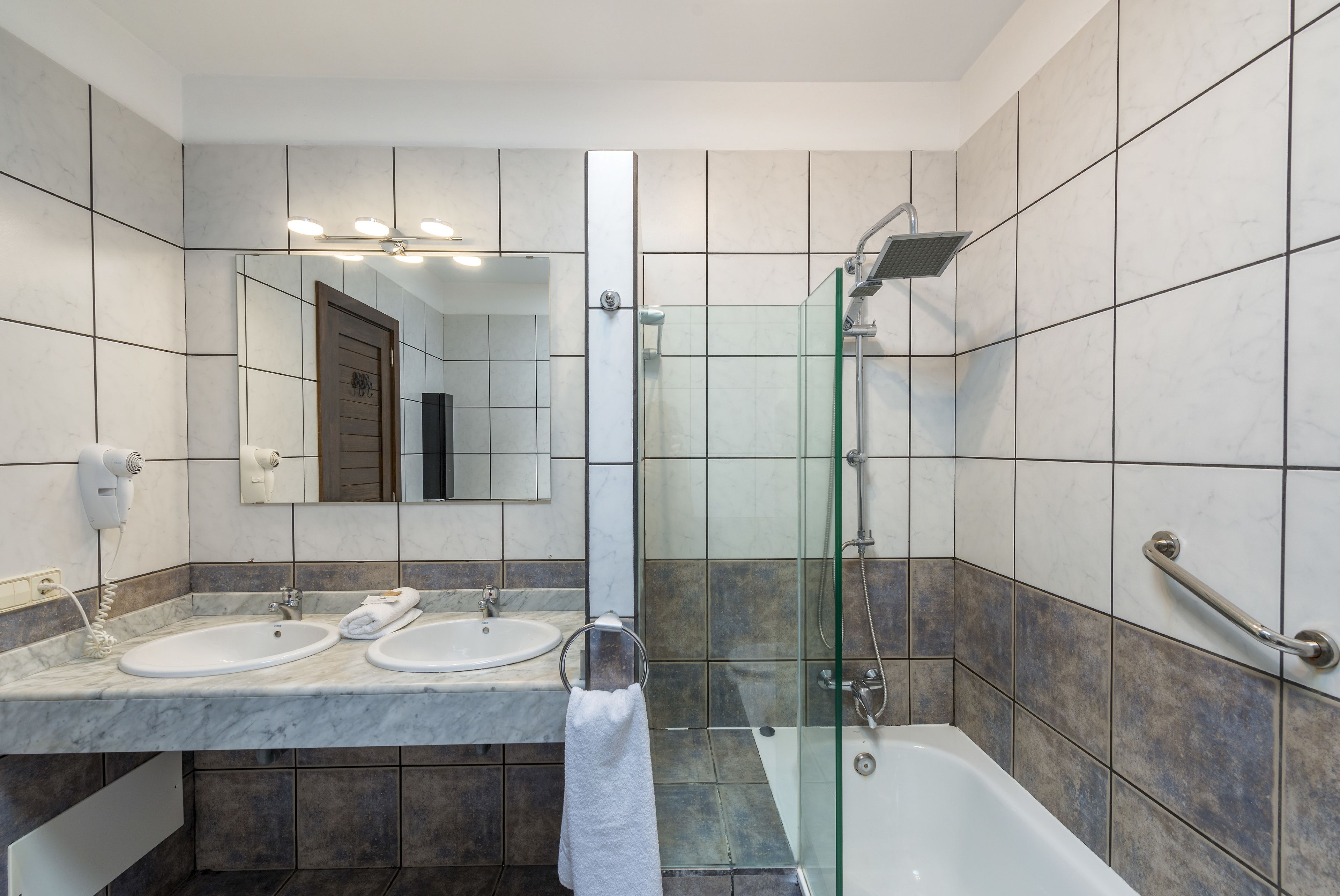 A modern bathroom with two sinks, a glass-enclosed shower, and a bathtub.