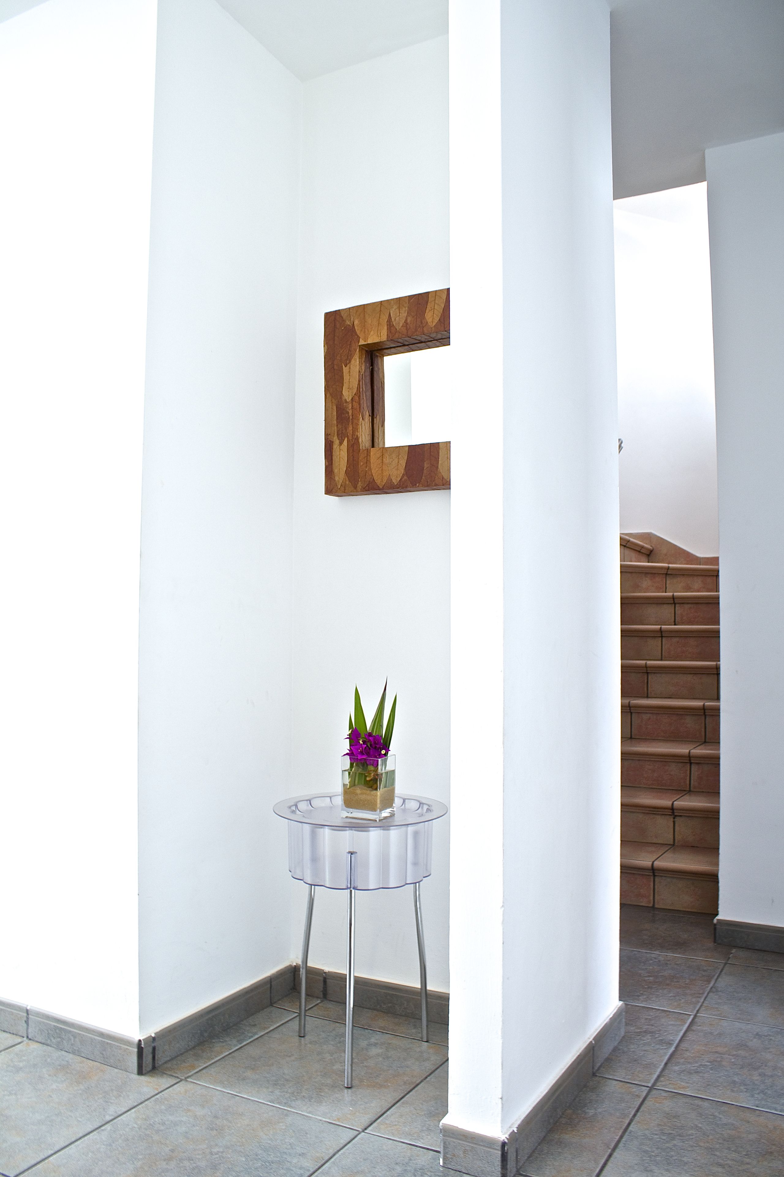 A corner of a room with a white wall, a wooden-framed mirror, and a small round table with a vase of flowers.