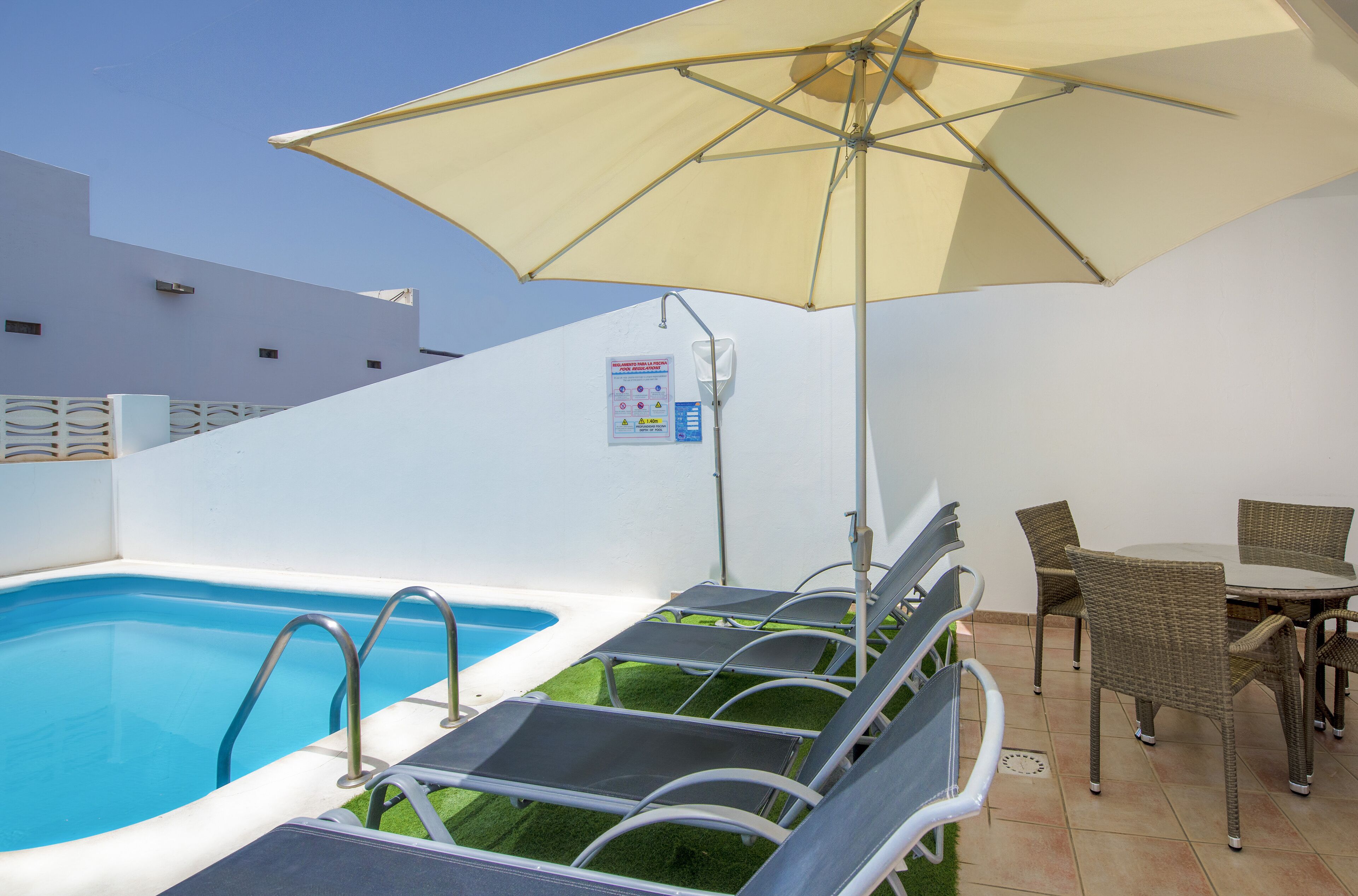 A pool area with lounge chairs, an umbrella, and a sign indicating pool regulations.
