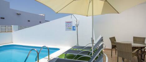 A pool area with lounge chairs, an umbrella, and a sign indicating pool regulations.