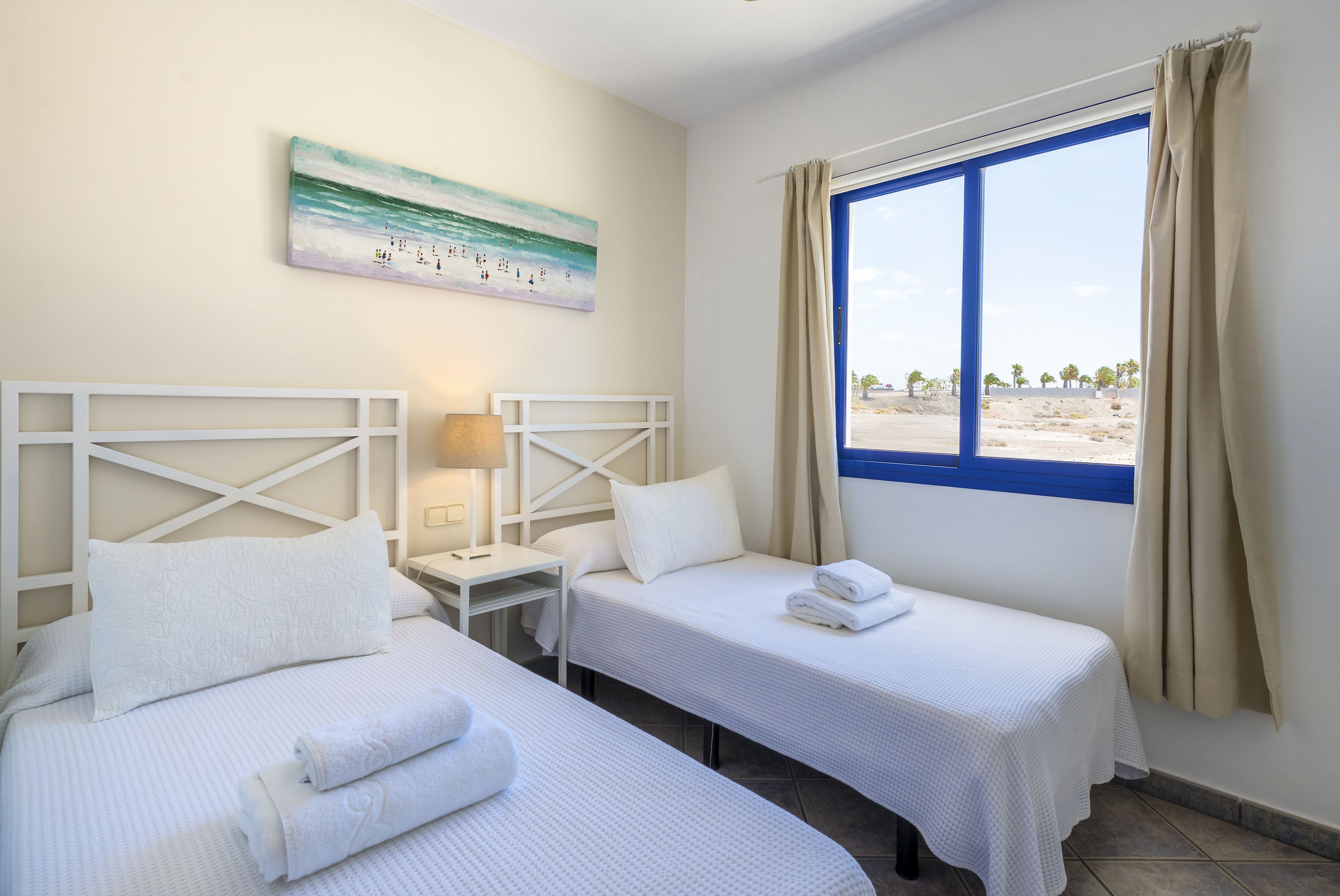 Une chambre d’hôtel avec deux lits, un tableau au mur, une fenêtre avec des rideaux et une vue sur la plage.