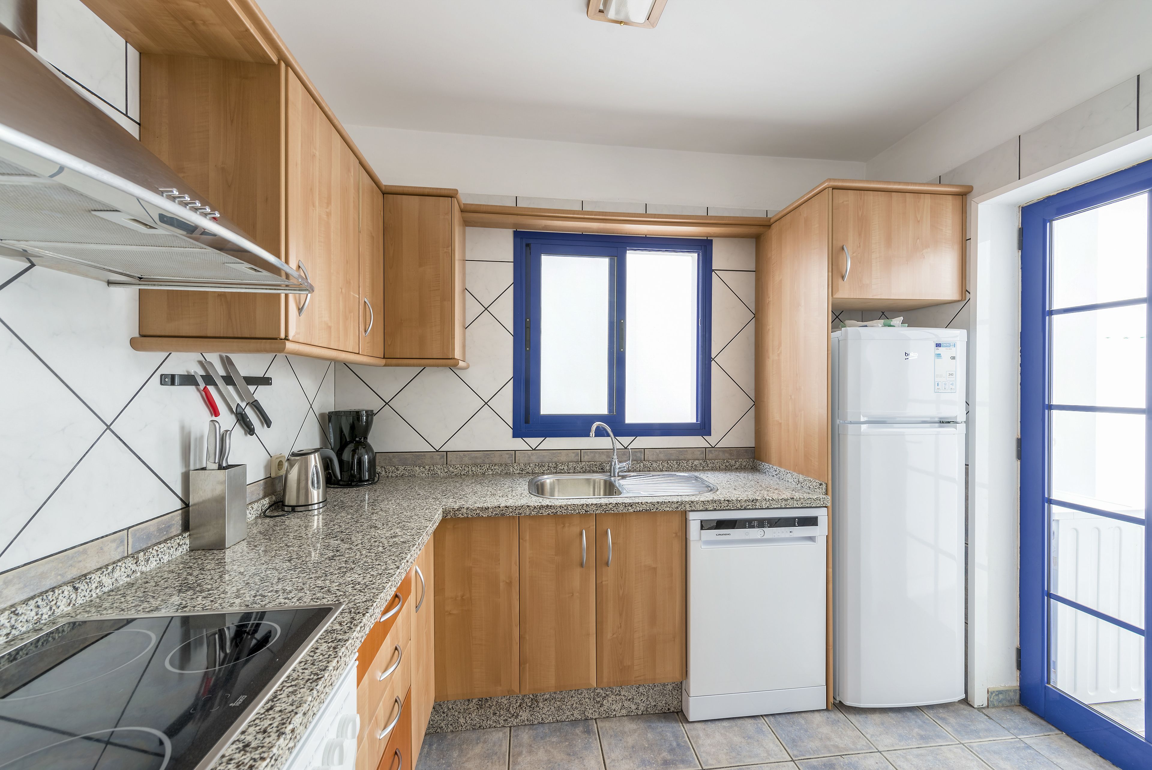 A kitchen with wooden cabinets, a built-in dishwasher, a stainless steel sink, and a window with blue shutters.