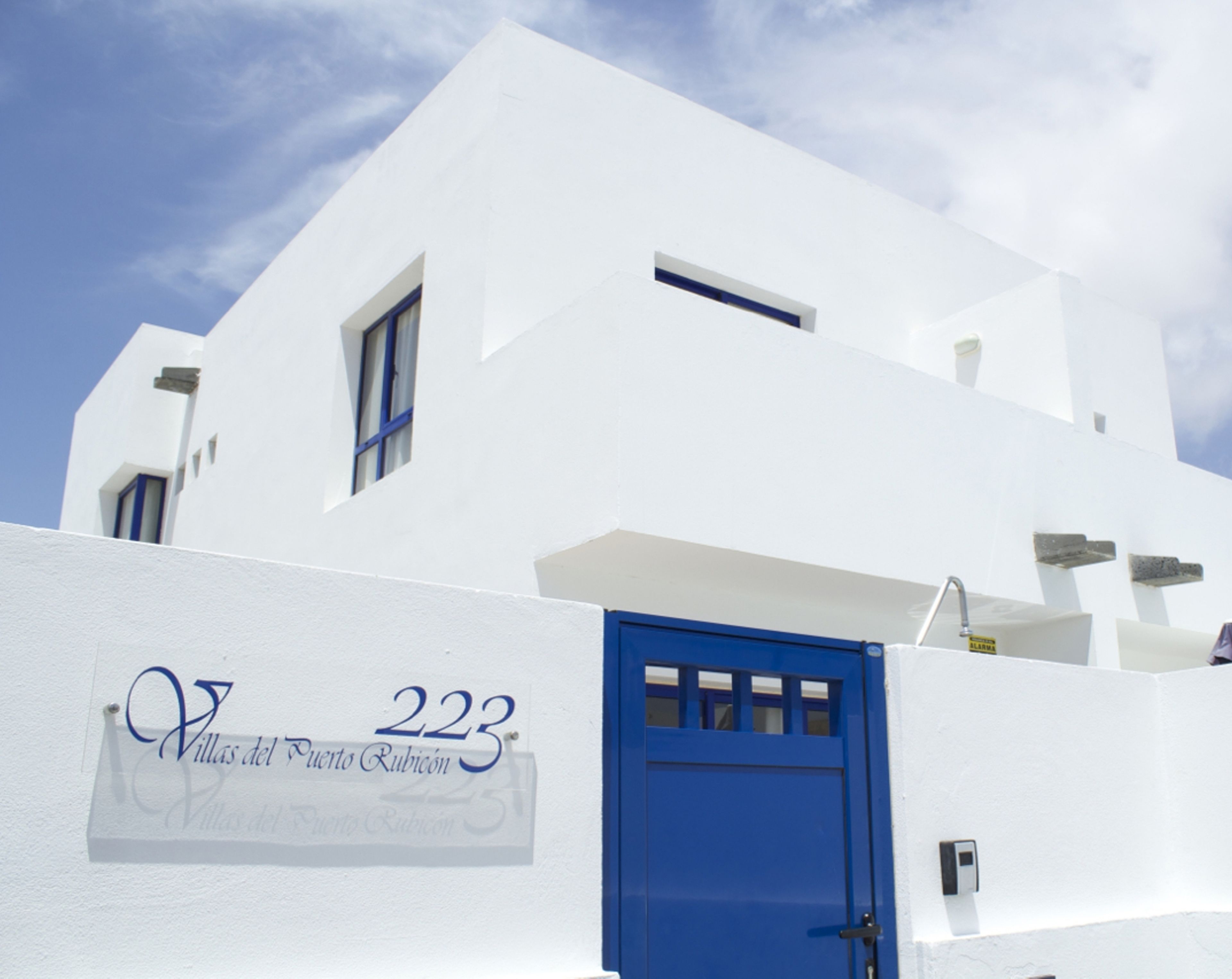A white building with a blue door and windows, labeled "Villas del Puerto Rubicon 223".