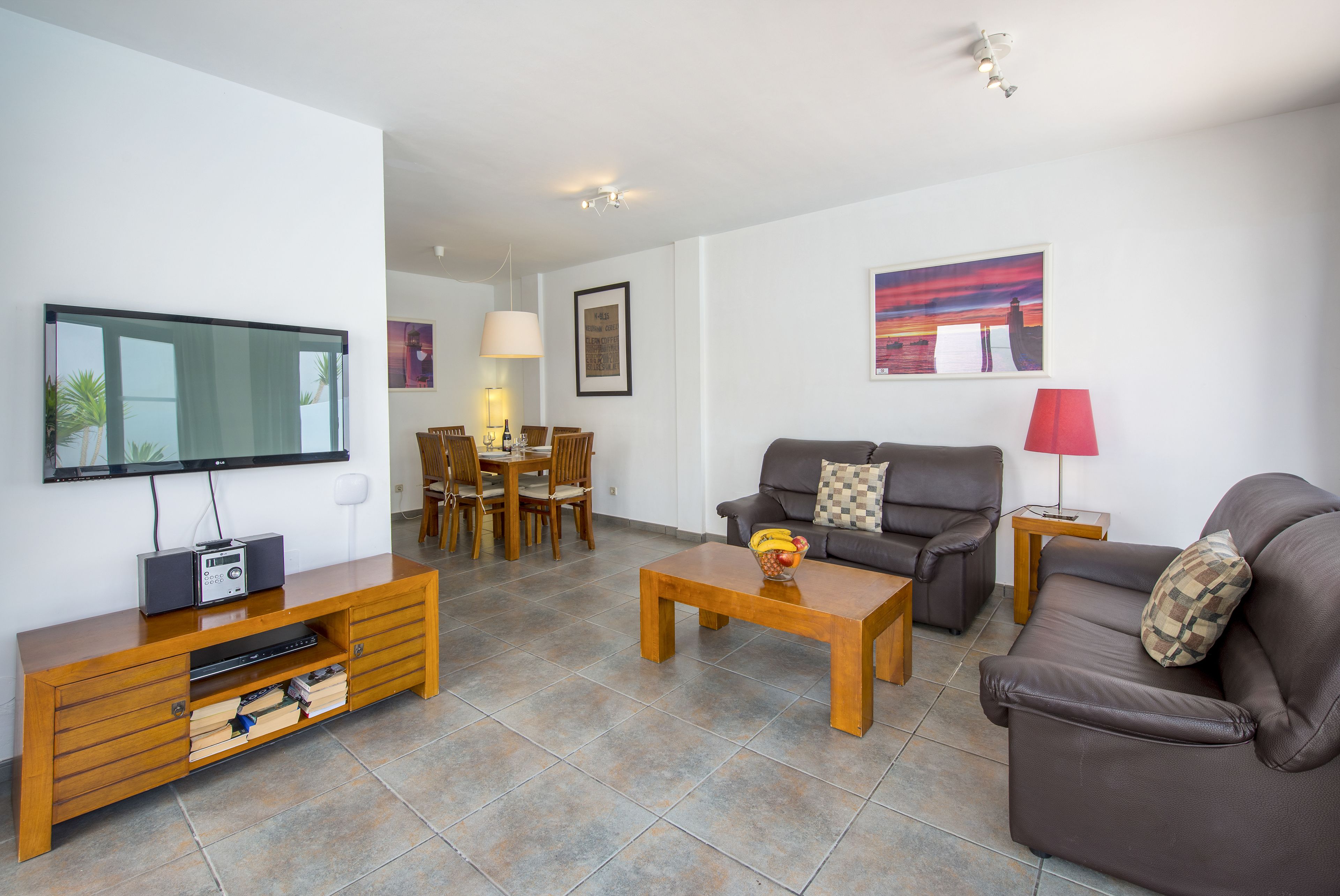 Een woonkamer met een televisie, bank, salontafel en een eethoek met stoelen en een tafel.