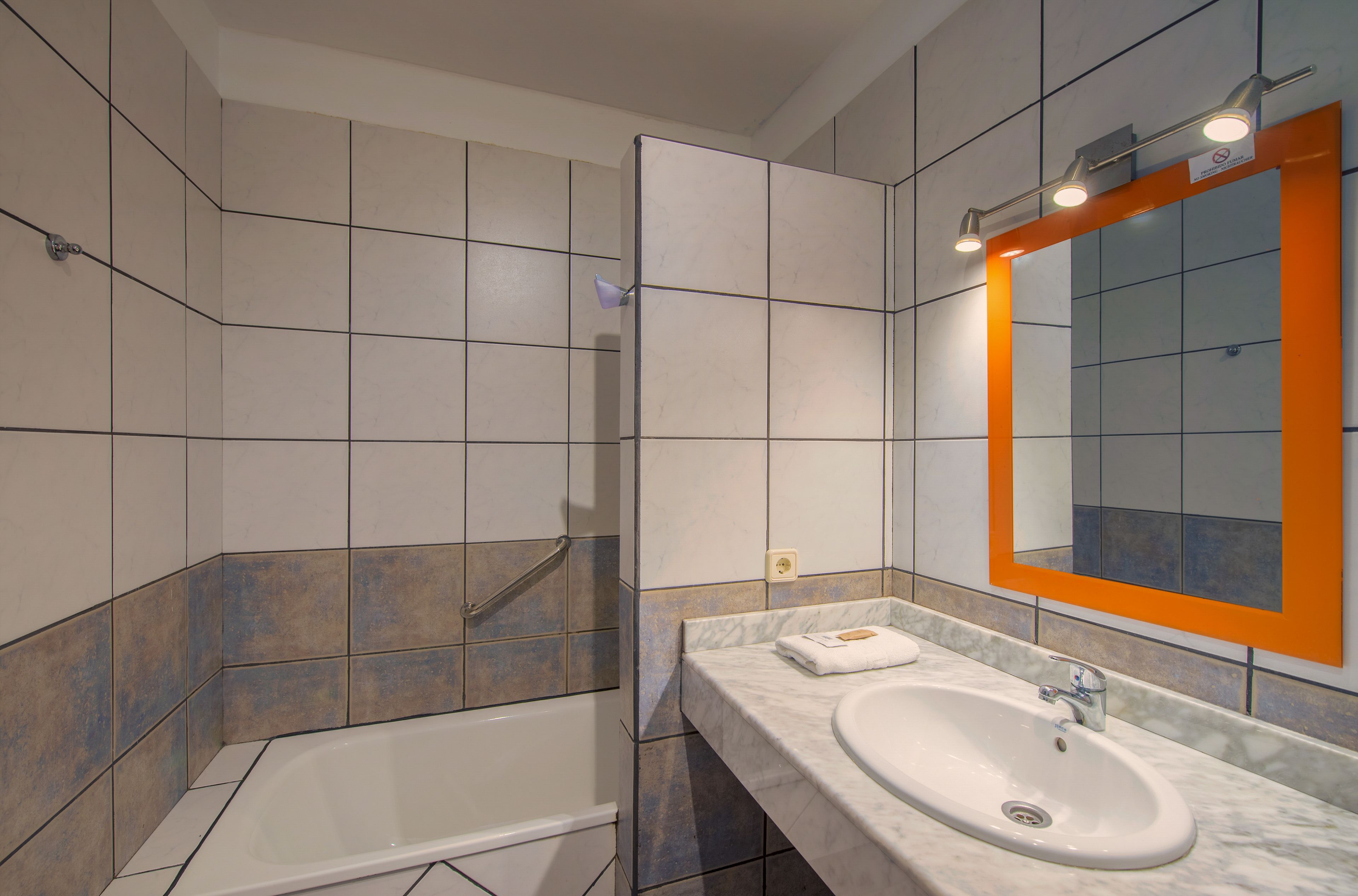 A modern bathroom with a bathtub, a sink, and a mirror with an orange frame.