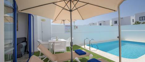 A poolside area with lounge chairs, a table, and umbrellas.