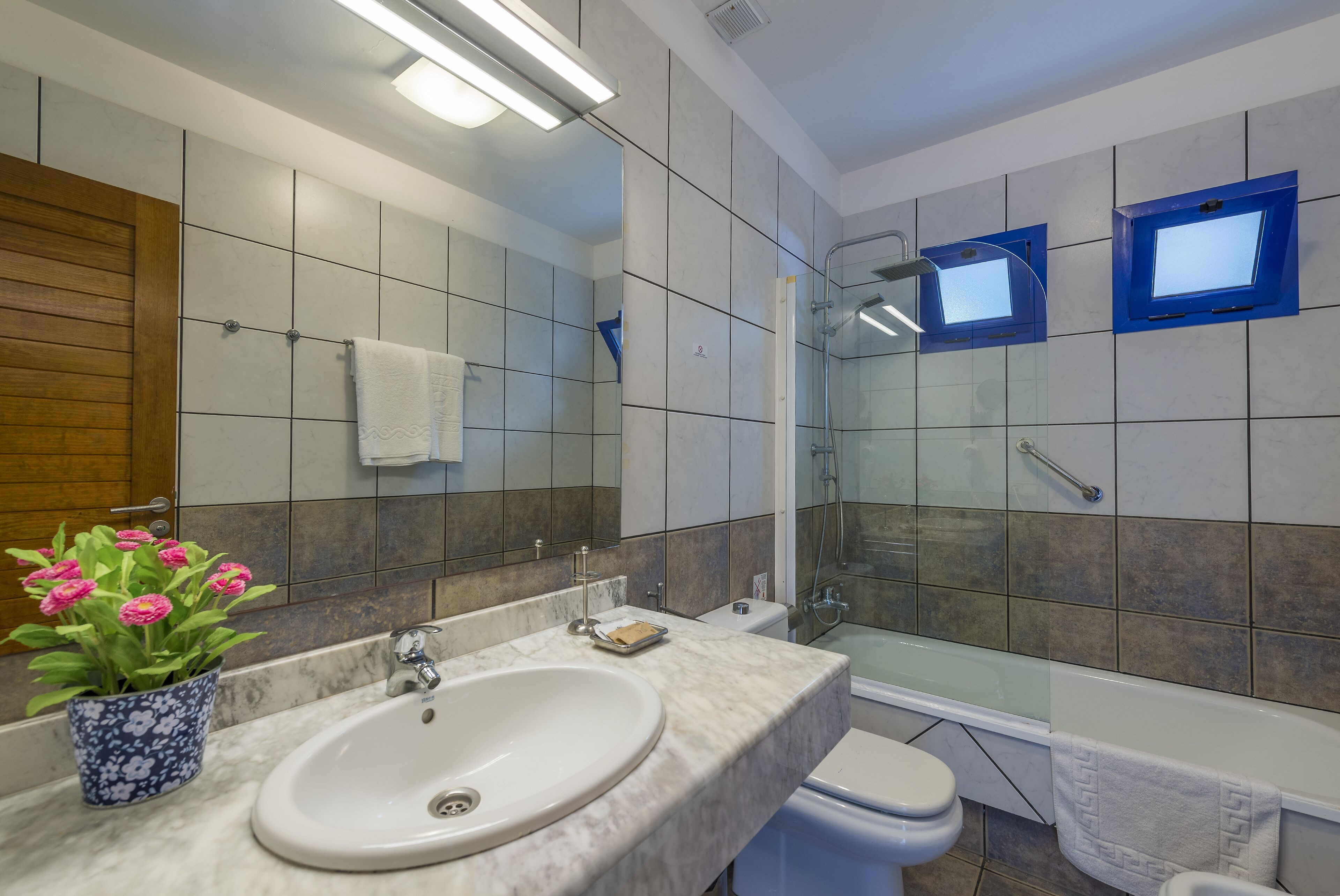 Un baño moderno con lavamanos de mármol, mampara de ducha de vidrio y panel de madera a la izquierda.