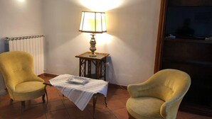 Ein Zimmer mit zwei gelben Sesseln, einem kleinen Tisch mit weißen Spitzen, einer Lampe und einer Heizung.