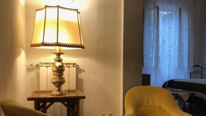 Ein Zimmer mit einer Lampe auf einem kleinen Tisch, einem gelben Sessel und einem Bett mit weißer Bettdecke.