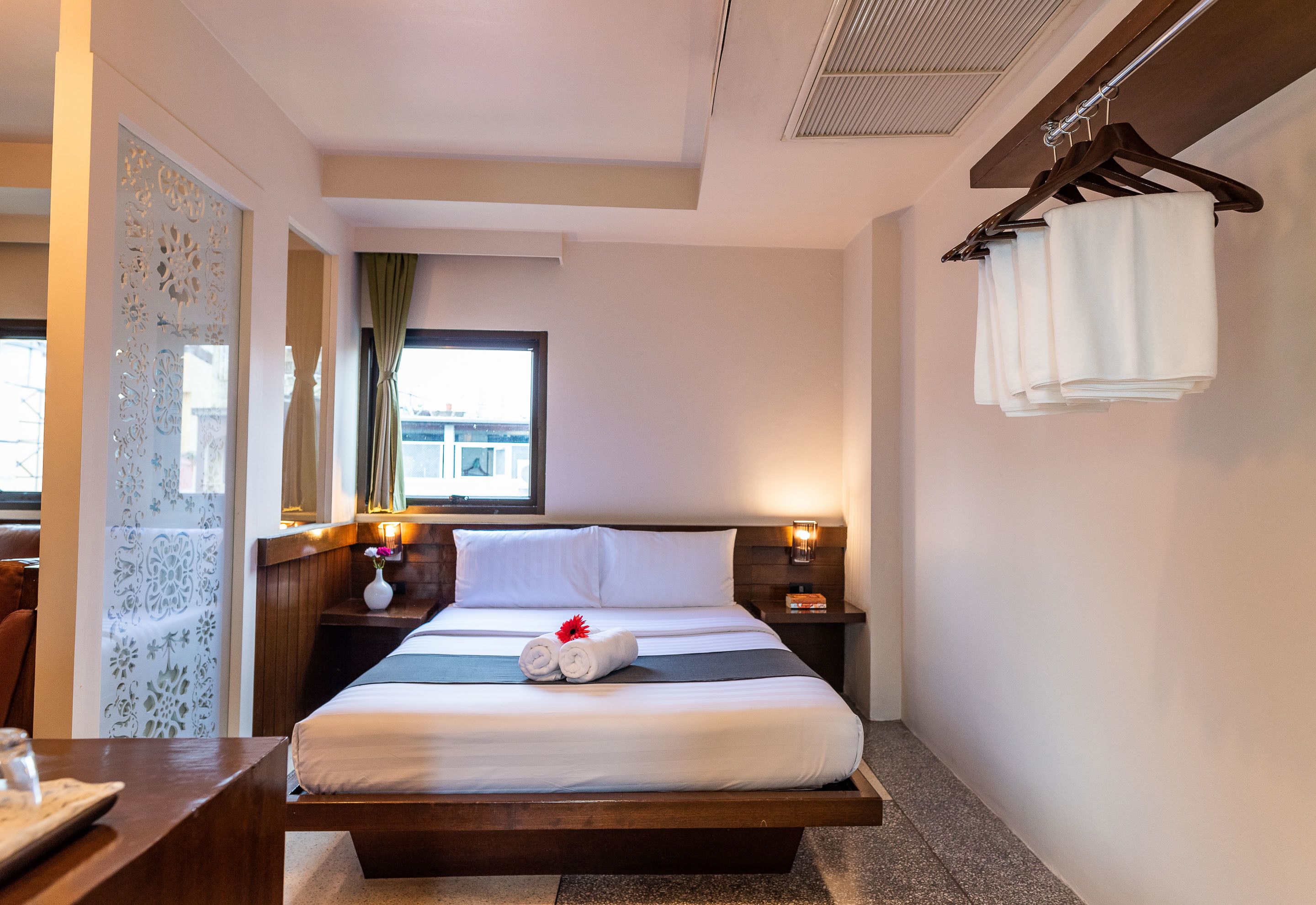 A hotel room with a bed, bedside tables, a window with curtains, a hanging towel rack, and a view of the city.