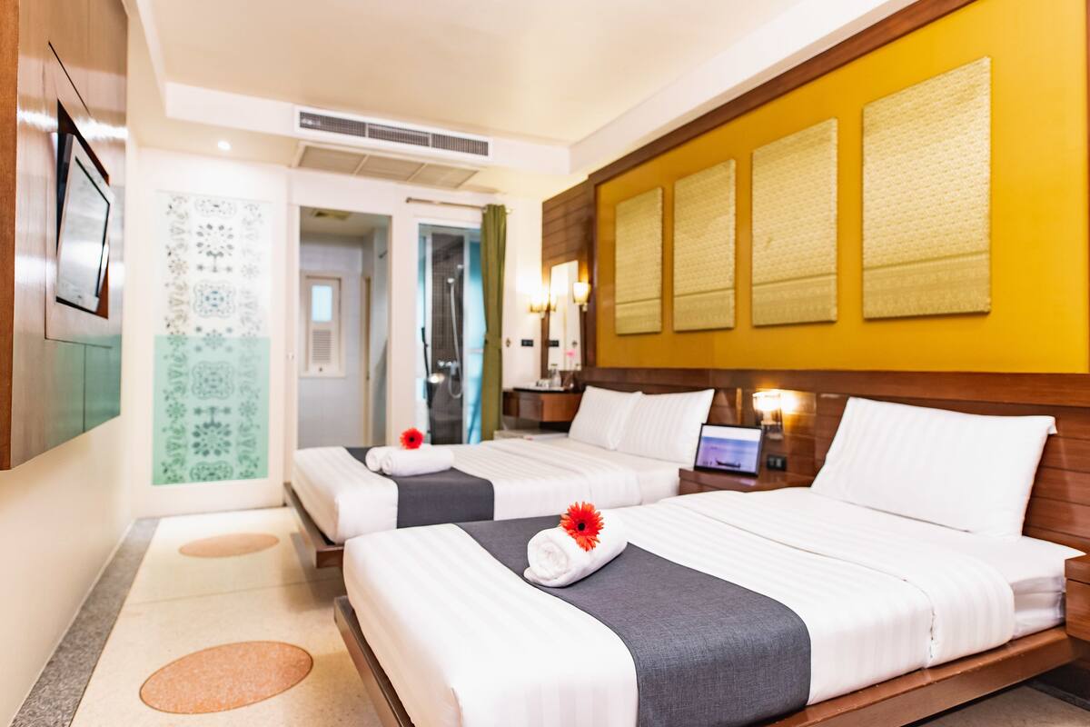 A hotel room with two beds, a TV, a bathroom, and a yellow accent wall.