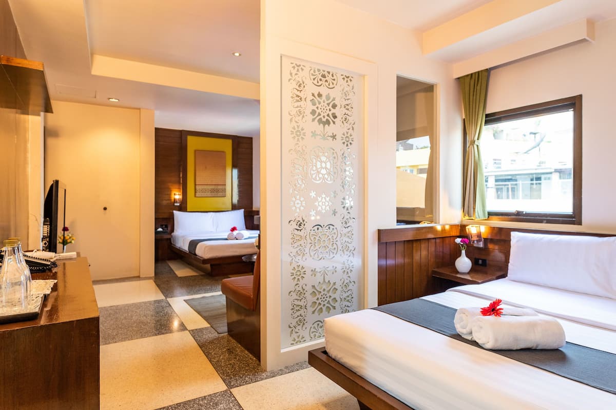 A hotel room with a bed, a desk, a chair, a decorative partition, and a window with curtains.