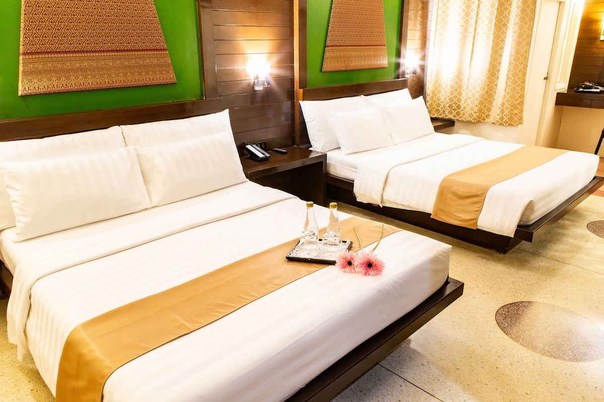 A hotel room with two beds, a bedside table with a phone, and a tray with bottles and flowers.