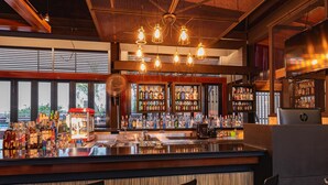 A bar area with a counter, multiple shelves of bottles, and a large television screen. - D&D Inn Khaosan (Bangkok)