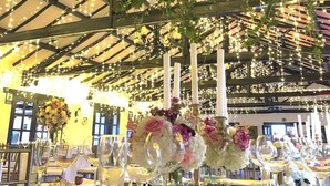 A banquet hall with tables set for a formal event, featuring floral centerpieces and string lights.