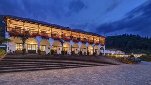 A large, multi-story building with a series of arches and balconies, featuring outdoor seating areas and a stone-paved entrance.