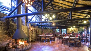 An outdoor dining area with stone walls, a fire pit, and wooden tables and chairs.