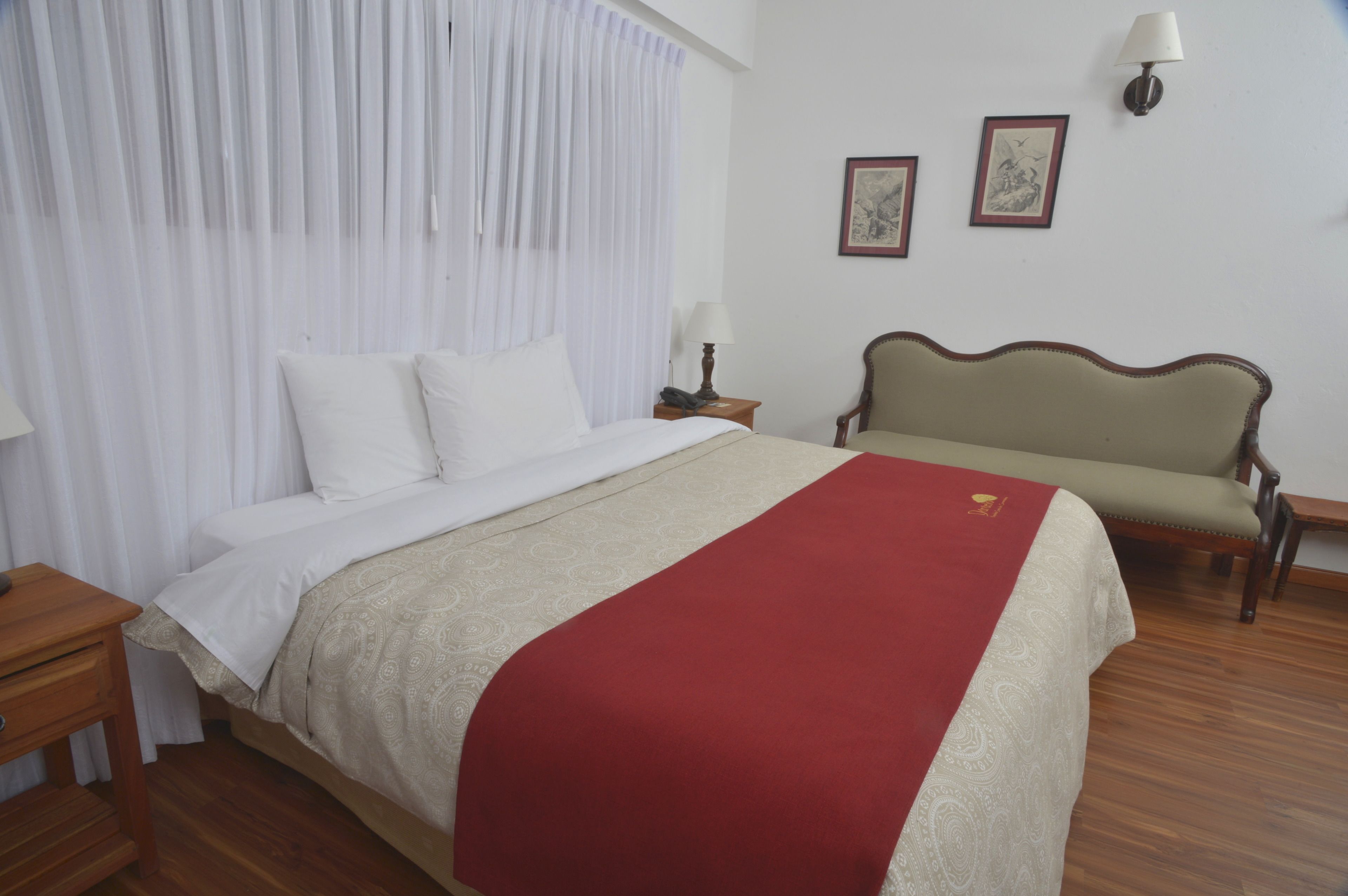 Habitación de hotel con cama, mesita de noche, silla y lámpara de pared.