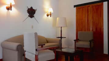 Una sala de estar con un sofá, dos sillones, una mesita y dos lámparas de pared.