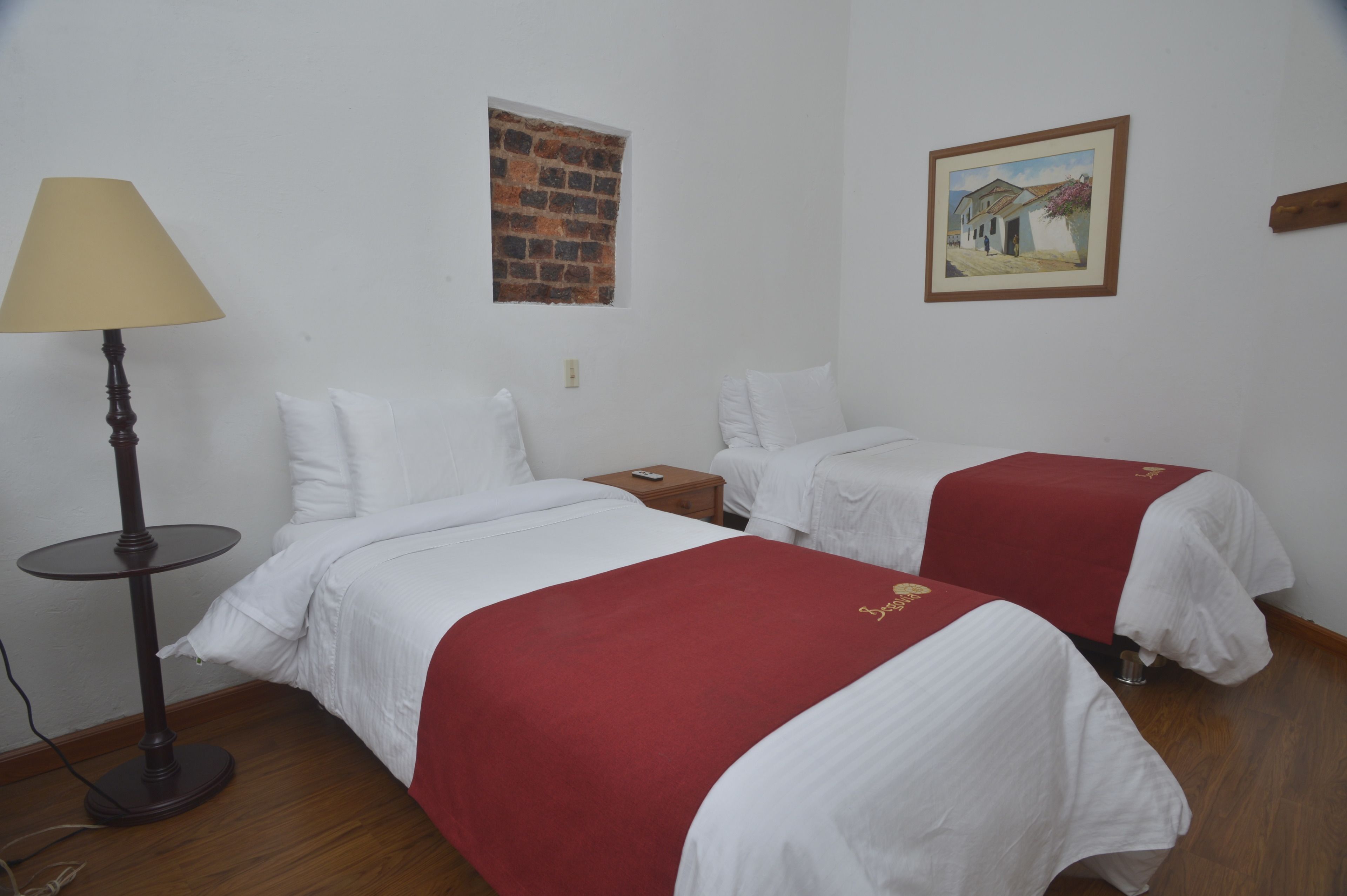 A hotel room with two beds, a lamp, a brick wall picture, and a framed picture on the wall.