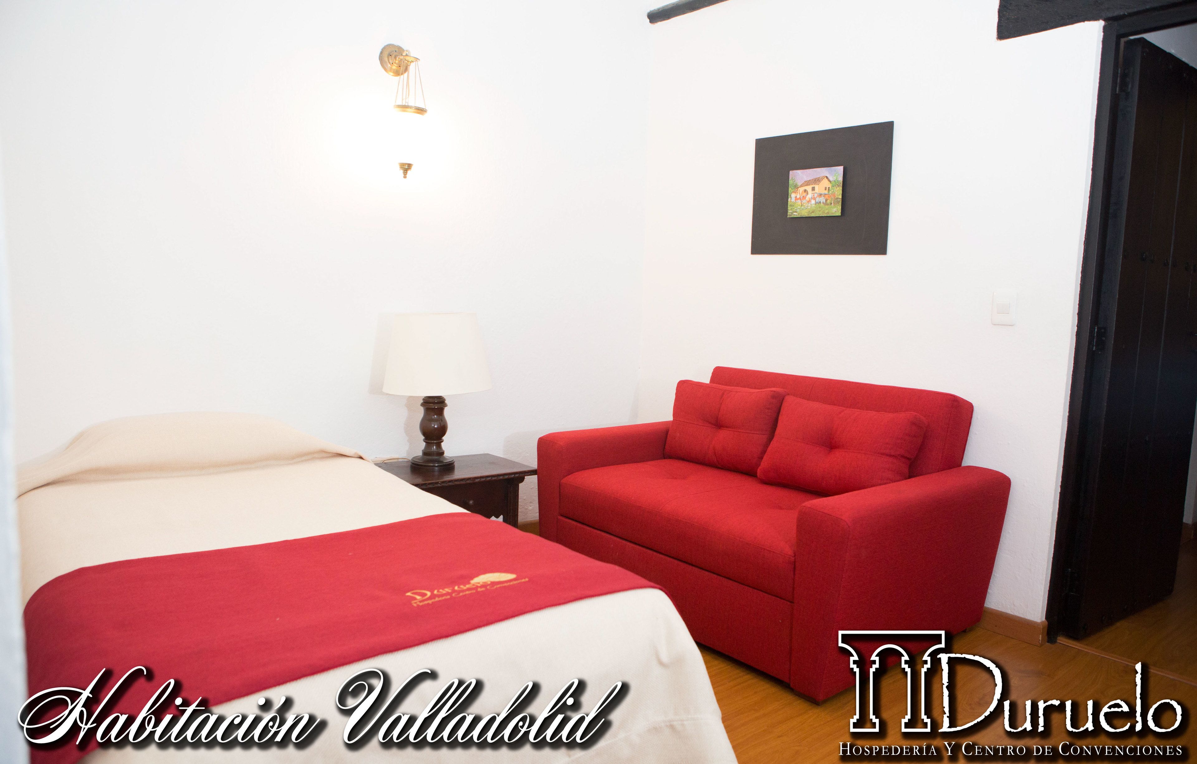 A hotel room with a bed, a red sofa, a lamp, and a framed picture on the wall.