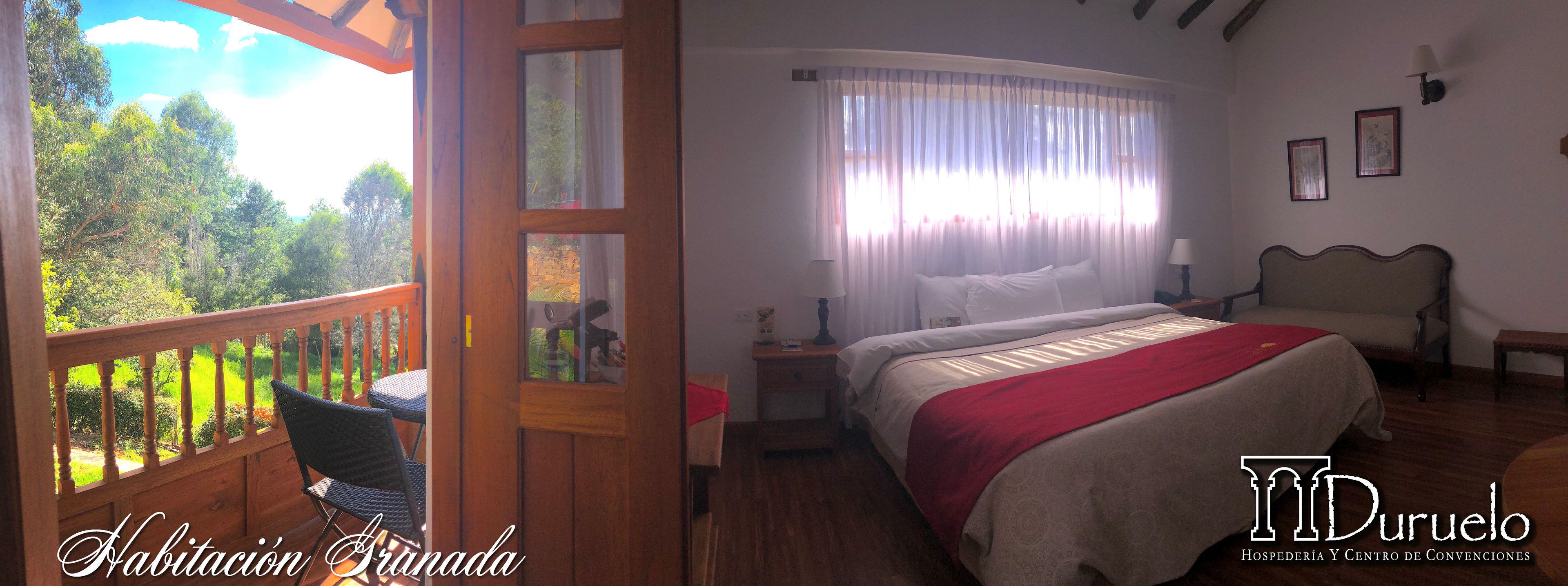 Un dormitorio con cama, mesita de noche, lámpara y vistas al exterior.