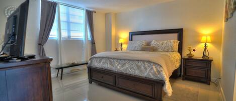A bedroom with a bed, bedside tables, a TV, and a window with curtains.