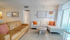 A modern living room with a brown leather sofa, a white sectional sofa with orange cushions, a round coffee table, and two wall-mounted lamps.