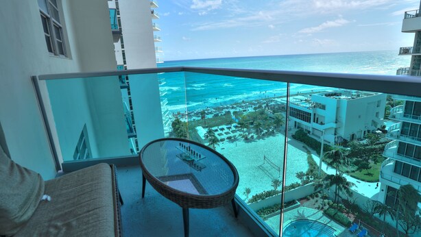 A balcony with a glass railing overlooking a beach and ocean.