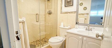 Un baño moderno con ducha de vidrio, inodoro y lavamanos con espejo.