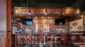 A bar area with wooden bar counters, multiple seating options including bar stools and tables, and a variety of bottles and glasses on the shelves. - Bicycle Street Inn (Mackinac Island)