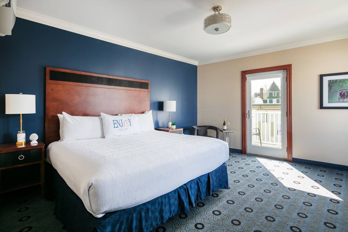 A hotel room with a large bed, two bedside tables, a nightstand, a door with a view, and a patterned carpet.