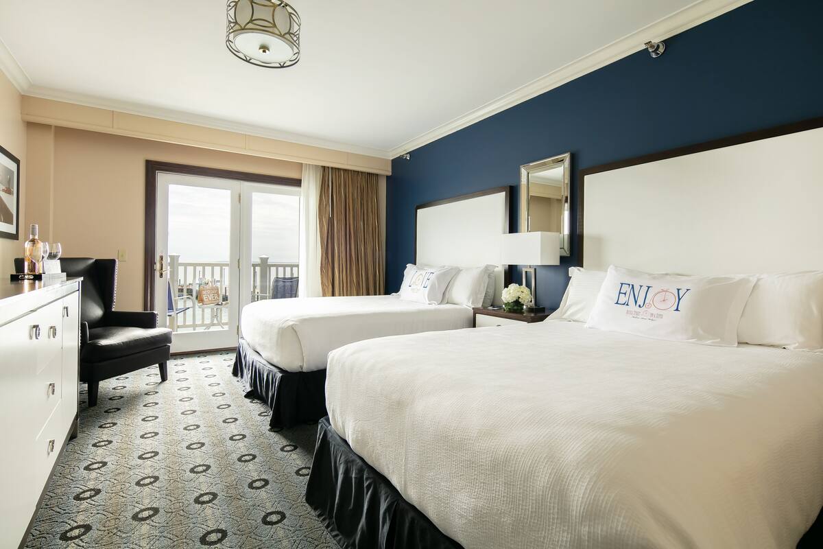A hotel room with two beds, a dresser, a chair, a balcony with a view, and a large mirror.