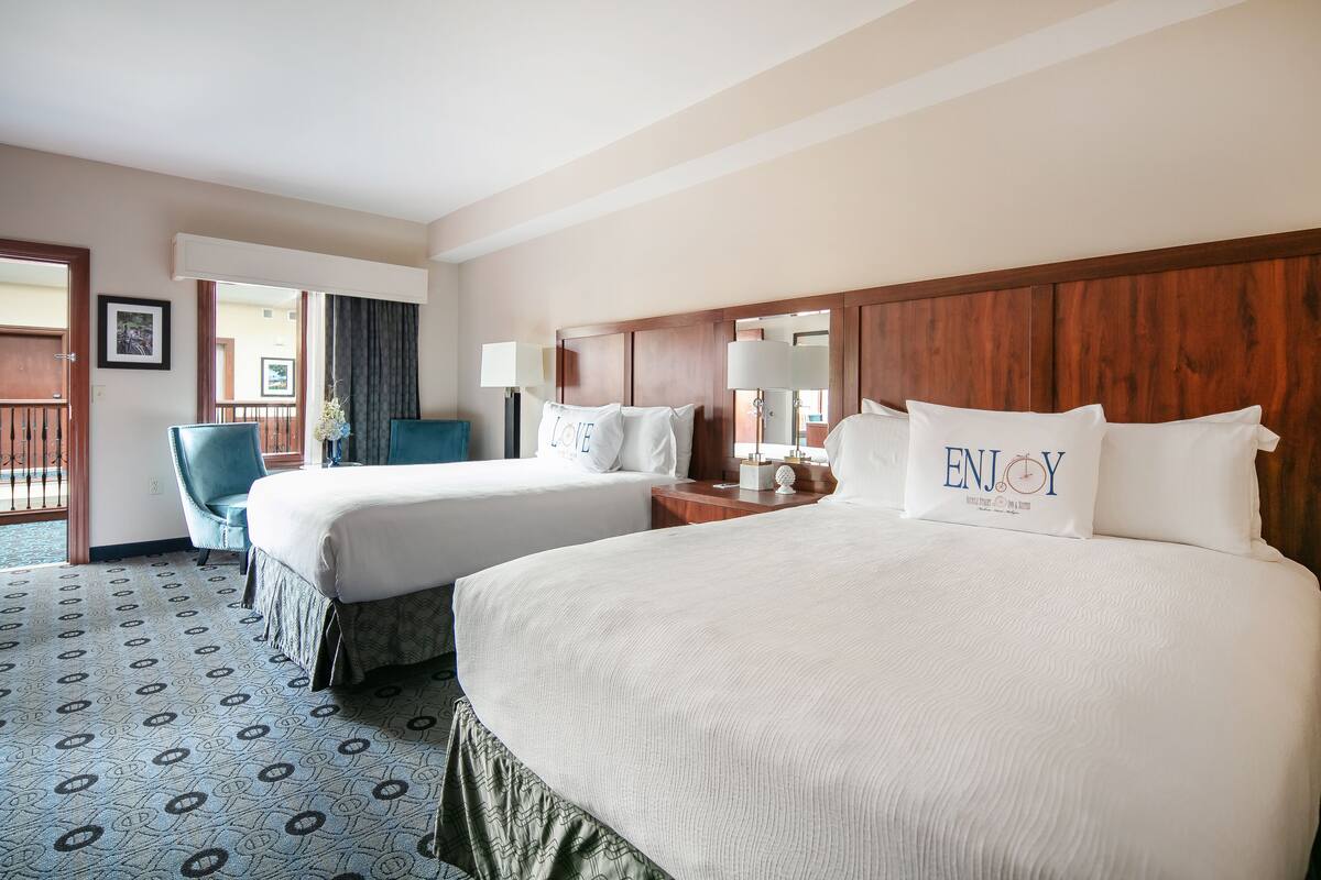 A hotel room with two beds, a chair, a wooden headboard, and a patterned carpet.