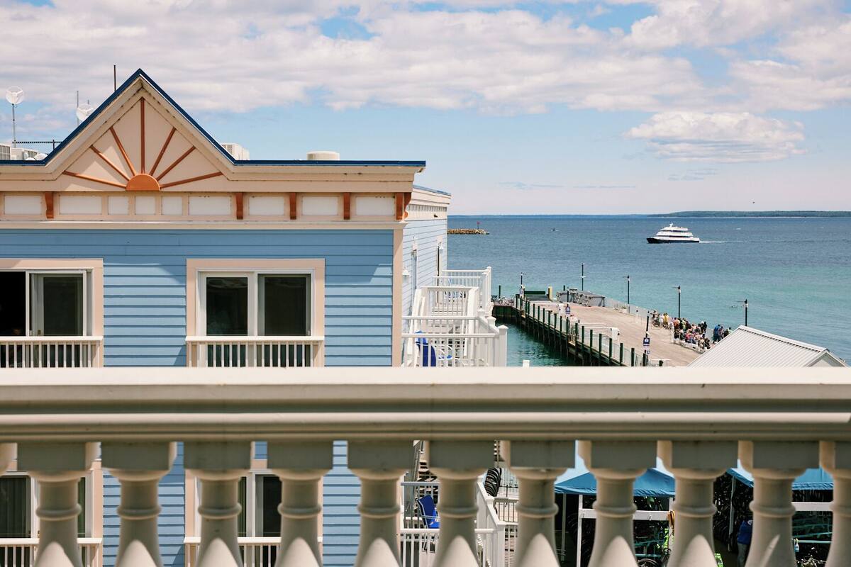 A coastal view with a pier extending into the water, a blue building with a sun motif, and a boat in the distance.