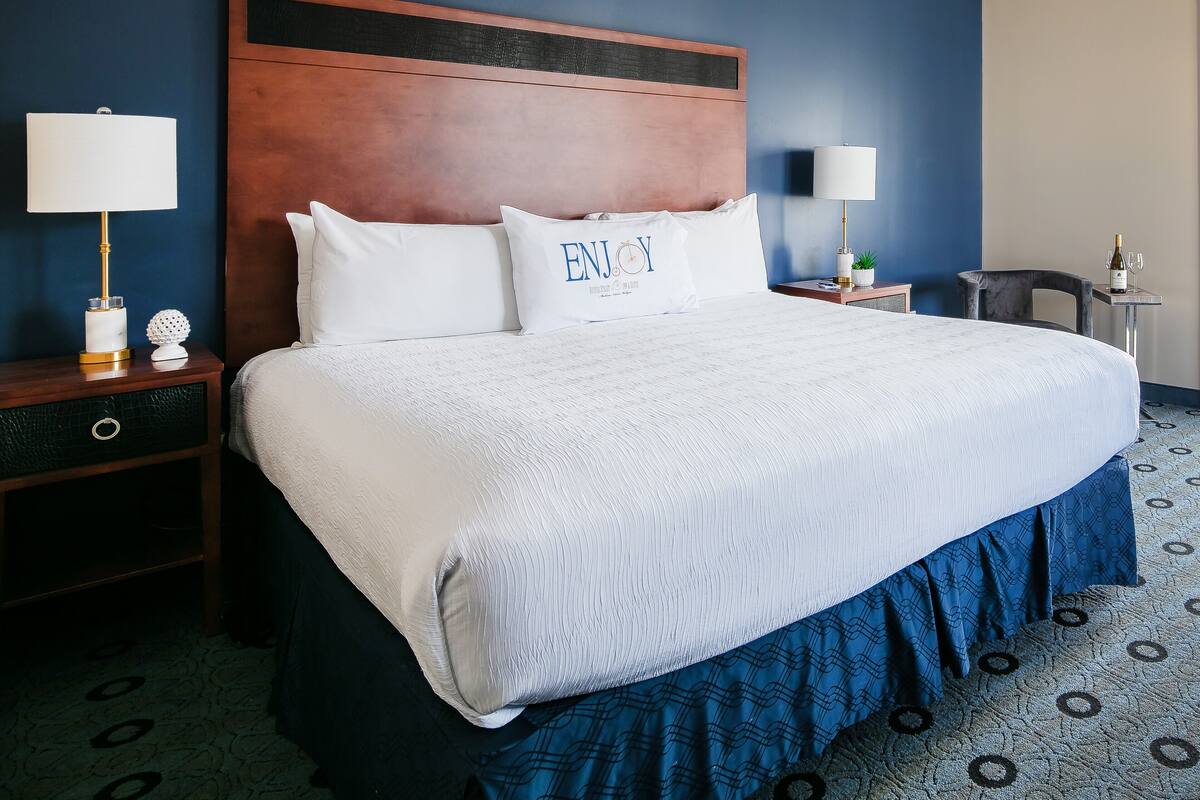 A hotel room with a large bed, two bedside tables, a nightstand, a headboard, and a ceiling light fixture.