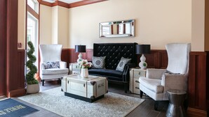 A living room with a black tufted sofa, white armchairs, a white coffee table with a vintage suitcase, and a mirror on the wall. - Bicycle Street Inn (Mackinac Island)