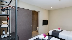 A hotel room with two beds, a TV, a bookshelf, and a bathroom visible through an open door.