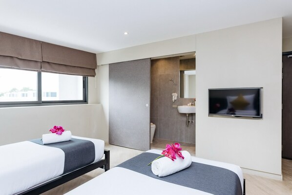 Habitación de hotel con dos camas, un televisor, un baño con lavamanos y un ventanal grande.