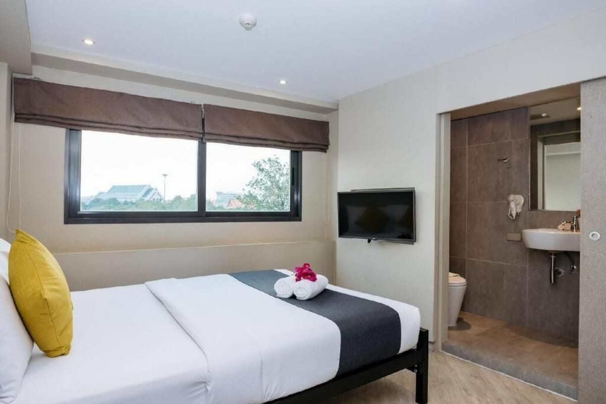 Una habitación de hotel con cama, televisor, baño con lavamanos y ventana con vistas.
