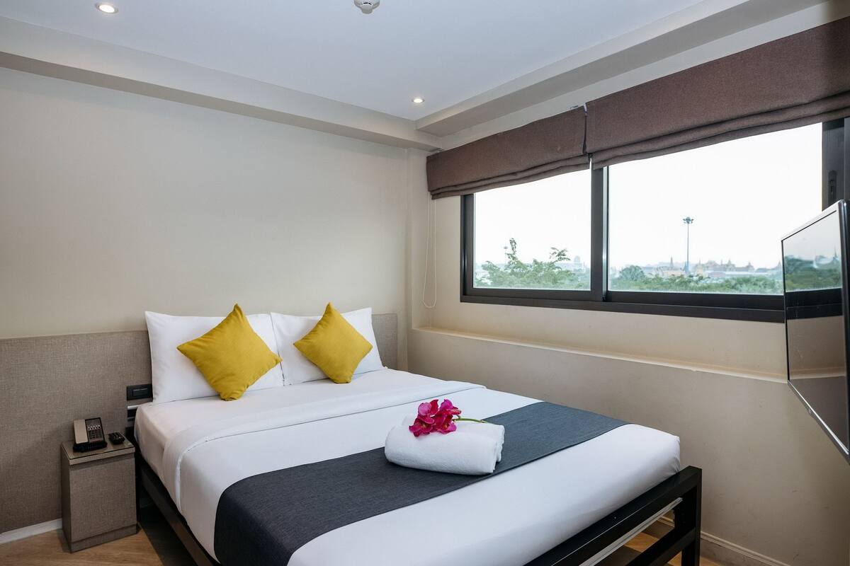 A hotel room with a bed, a nightstand, a telephone, and a window with a view.
