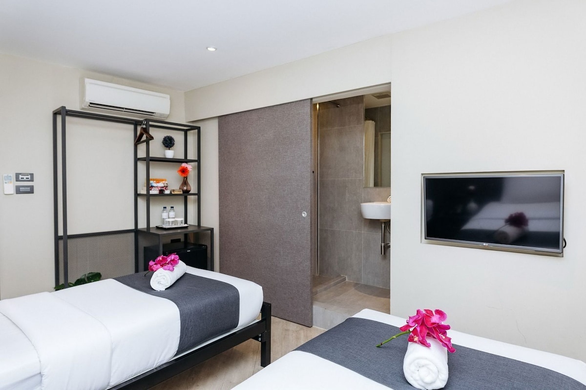 Habitación de hotel con dos camas, televisión, ducha y un estante con artículos de aseo.
