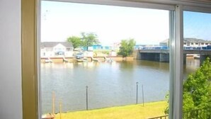 A view from a window overlooking a calm river with boats, a bridge, and buildings in the background. - Edgewater Resorts - Edgewater Cottages (Wasaga Beach)