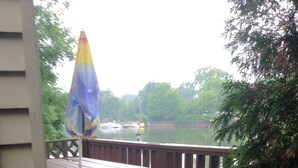 A wooden deck with a picnic table and a blue and yellow umbrella, overlooking a body of water. - Edgewater Resorts - Edgewater Cottages (Wasaga Beach)