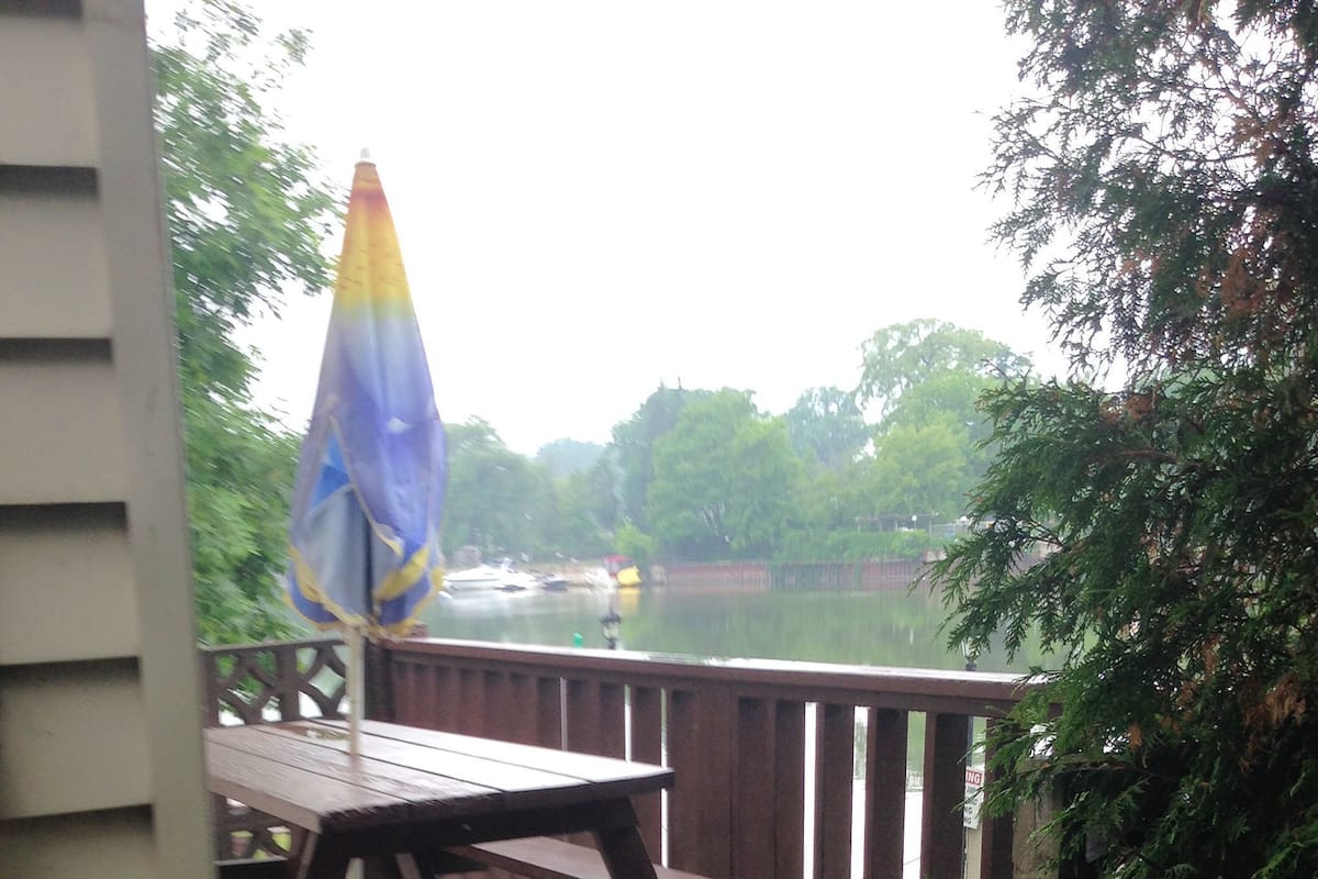 A wooden deck with a picnic table and a blue and yellow umbrella, overlooking a body of water.