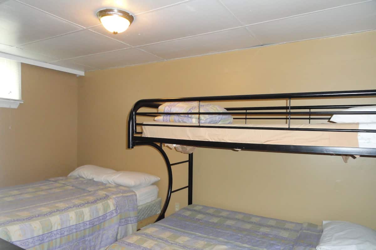 A dormitory room with two single beds, a bunk bed, and a ceiling light fixture.