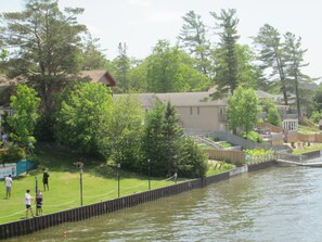 A riverside view with a wooden dock, a grassy area, and a building with a balcony. - Edgewater Resorts - Edgewater Cottages (Wasaga Beach)