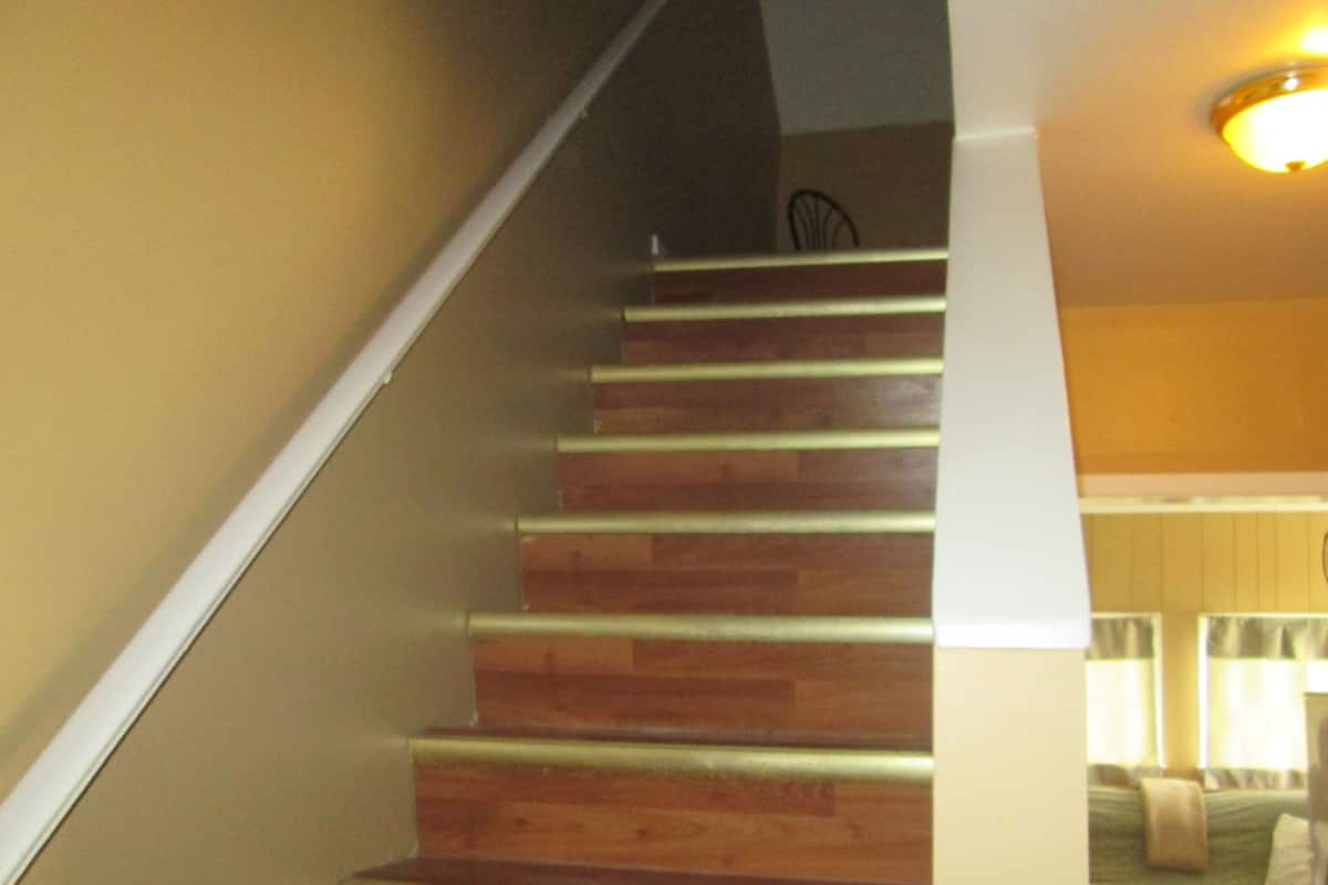 A wooden staircase with white handrails leading to a room with a bed and a window.