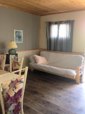 A cozy room with a wooden ceiling, a sofa, a table with chairs, and a lamp.
