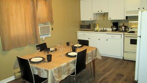 Comedor con una mesa dispuesta para cuatro, armarios blancos, microondas, cafetera y estufa.